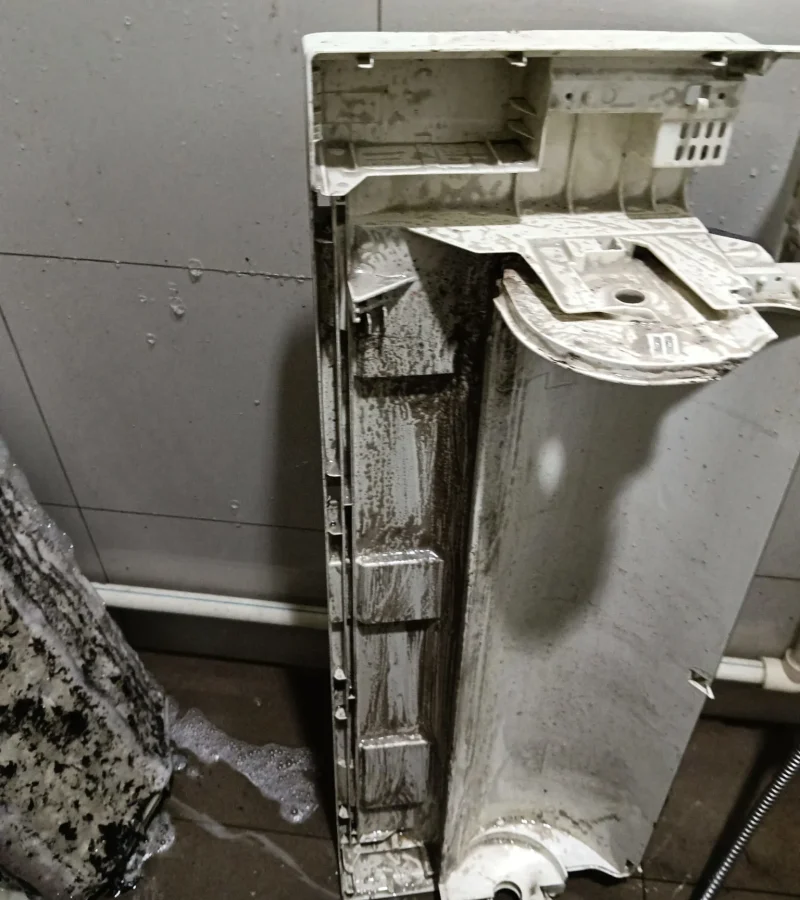 Plastic air conditioner back casing covered in soapy foam and dirt residue during a chemical overhaul.