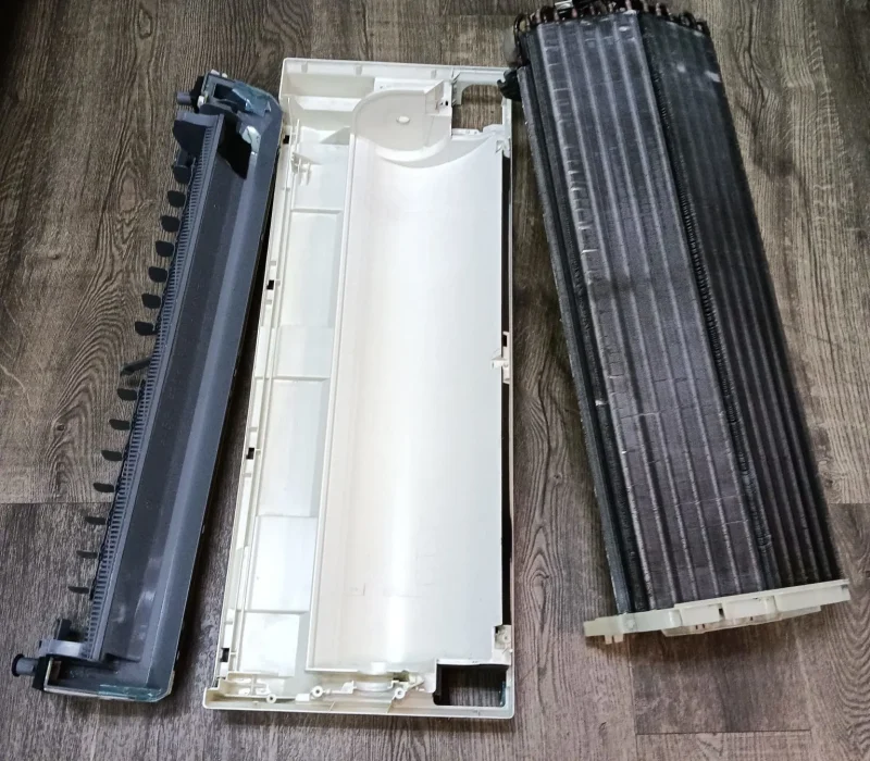 Washed air conditioner covers and filter frames leaning against a railing outside to air dry.