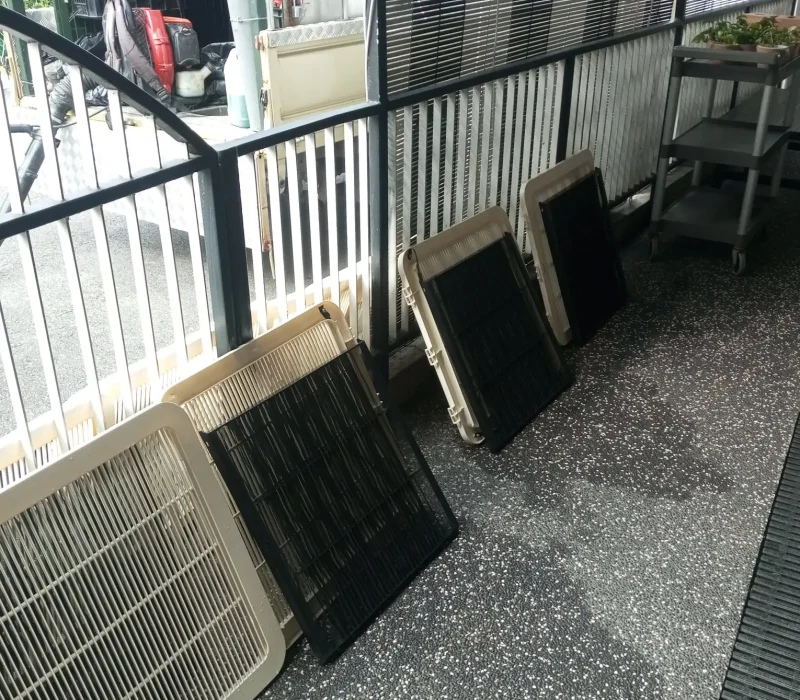 Washed air conditioner covers and filter frames leaning against a railing outside to air dry.